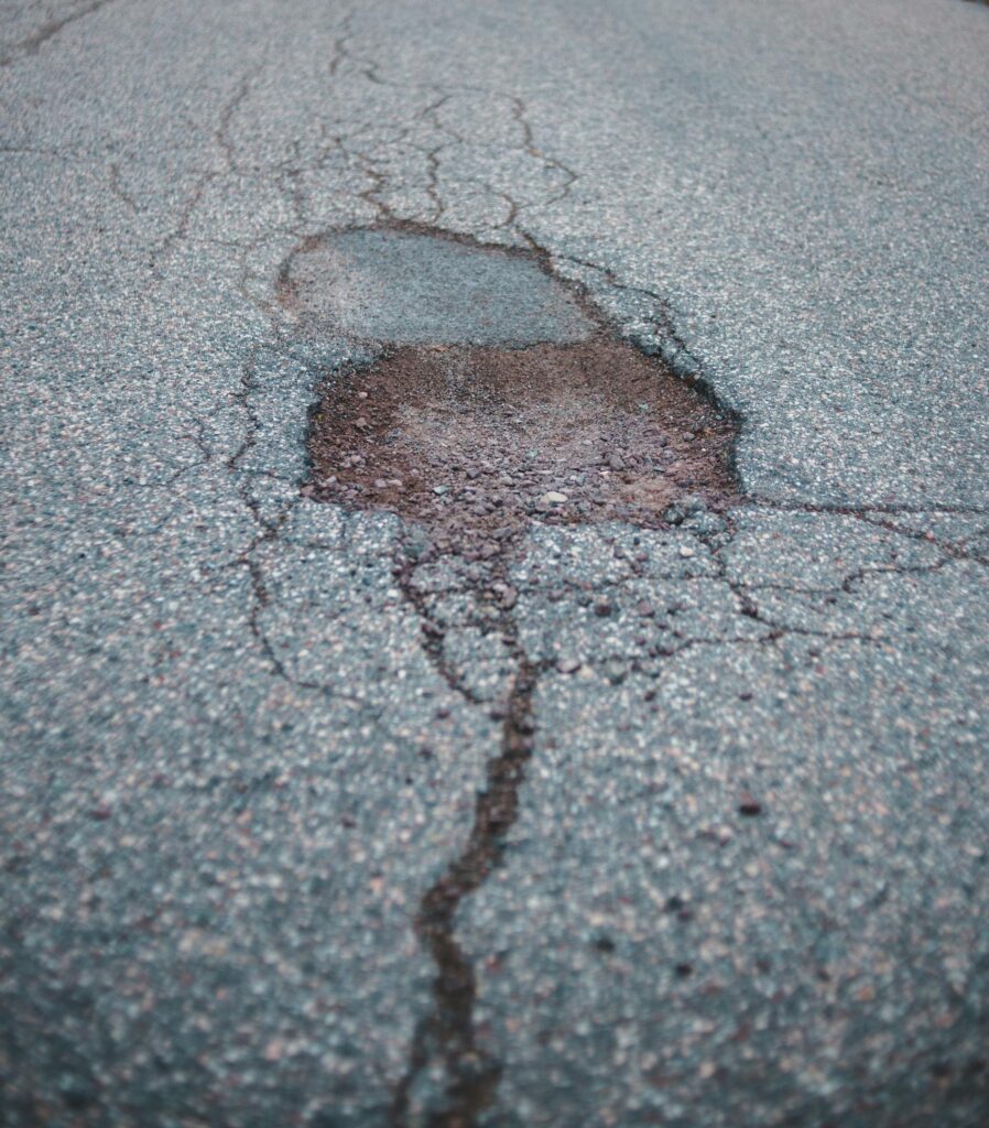 Empty rural road with a large pothole, leading through a tranquil and desolate wooded area.