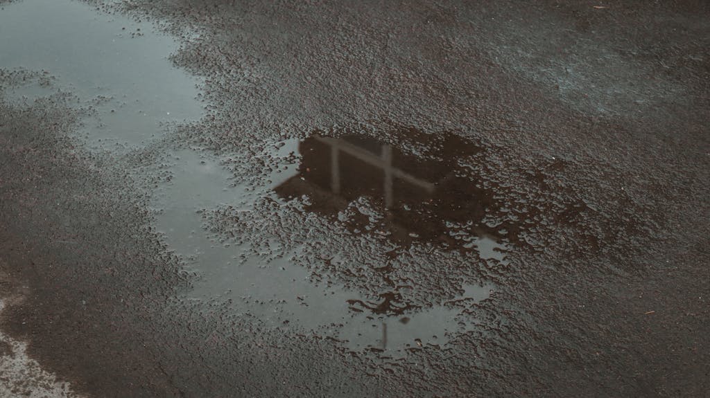 Rain puddle on asphalt with reflection of structure, creating a moody scene.