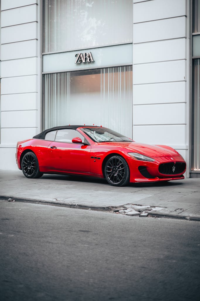 Stylish red convertible parked in city street with Zara store in background, chic urban scene.